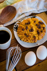 Delicious cornbread with chocolate chips, placed in a white porcelain dish and composed with eggs, wooden spoon, whisk, white cloth and a cup of coffee
