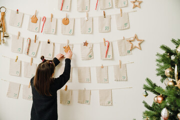 Little girl opening gift of handmade advent calendar hanging on wall at home