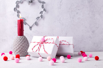 Postcard with  wrapped presents, heart, red burning candle, pink and red pom poms against  grey  textured  wall.  St. Valentines day postcard. Place for text.