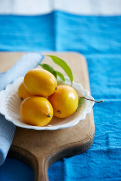 four whole meyer lemons in a bowl with lemon leaves on a cutting board, Canada