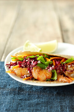 Single Serving Shrimp Taco with Red Cabbage, Carrot and Cilantro on Corn Tortillas with Lime Slices on Wooden Background
