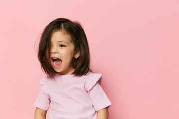 a cute little preschool girl on a pink background in a pink T-shirt is screaming loudly and waving...