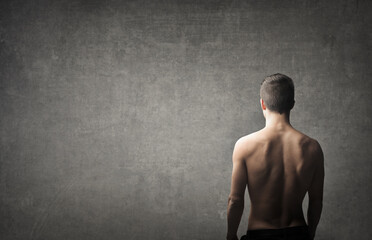 young man bare back from behind in front of a wall