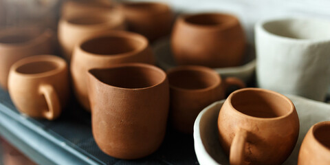 A close-up of various drying clay tableware on a shelf. A pottery studio concept. Craftmade dishes, bowls, pots, mugs of different colors. Cozy view. workshop with ceramic dishware