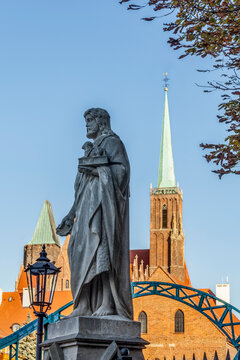 Statue of St. John the Baptist on Tumski Bridge with the Church of the Holy Cross (Collegiate Church of the Holy Cross and St. Bartholomew) in the background; Wroclaw, Silesia, Poland