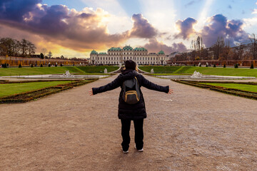 Young girl with arms outstretched in front of Schloss Belvedere in Vienna. Belvedere Castle at sunset. - 556746608