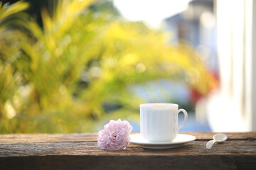 White coffee cup and pink rose on wooden table balcony outdoor