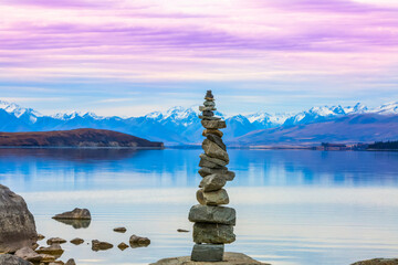 Beautiful views over the shoreline of New Zealand's Lake Tekapo at sunset. A stack of rocks sits lakeside; Lake Tekapo, Canterbury, New Zealand