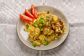 Rice chicken in teriyaki sauce garnished with green onions and tomatoes on a gray tablecloth.