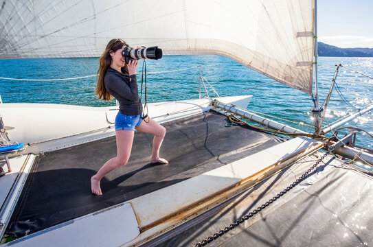 Fototapeta Woman standing on a catamaran taking photographs with a camera with a telephoto lens on a boat tour through the Abel Tasman National Park  Tasman, South Island, New Zealand