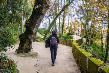 Fototapeta na wymiar Rear View Of A Woman Sightseeing In Sintra, Portugal. She Is Walking Through Some Nice Gardens Of The Regaleira Palace. Vacation And Travel Concept. Copy space