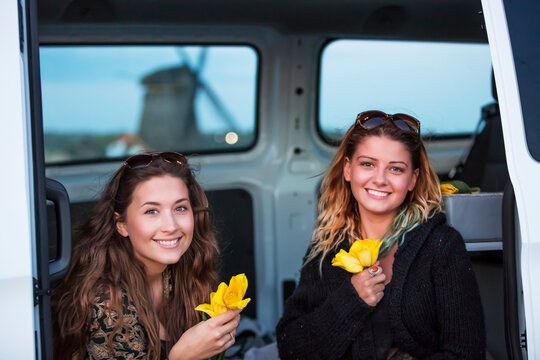 Two young women holding yellow tulips with a windmill in the background, Egmond aan Zee, Holland