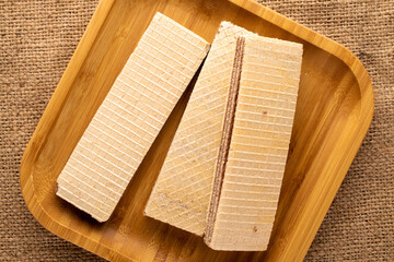 Three sweet chocolate wafers with bamboo plate on jute cloth, close-up, top view.