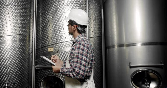 Large steel barrels for wine fermentation. Wine production plant. Steel wine distilling tanks. Winemaker looking equipment for distillation and fermentation at wine factory.