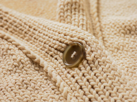 Extreme close-up of the collar and button on a cream-coloured knit sweater; Studio