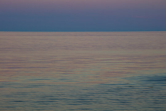Tranquil ocean water reflecting soft sunset colours; Perce, Quebec, Canada