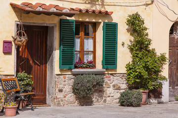 Traditional stucco home with wooden front door and window with green shutters on a sunny day in the town of Cortona; Arezzo, Tuscany, Italy