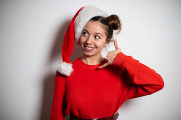 Portrait of young attractive brunette girl with two bundles in red pullover and Santa hat showing call me symbol