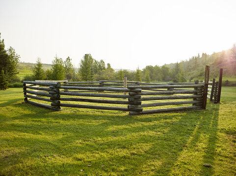 Empty paddock with a split rail fence on a grassy field surrounded by trees with shadows from the sunlight, Historic Cochrane Ranche Park; Cochrane, Alberta, Canada