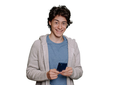 Excited schoolboy in light hoodie and grey t-shirt holds phone looks at camera toothy smiling against transparent background. Brunette guy happy with new smartphone. Mockup, youth, communications.