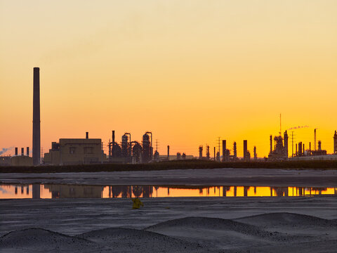 Golden sunlight behind the silhouetted structures at oil sand production facility (Suncor Energy) at sunset; Fort McMurray, Alberta, Canada