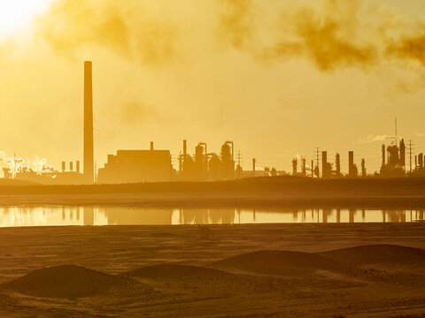 Golden sunlight behind the silhouetted structures at oil sand production facility (Suncor Energy) at sunset; Fort McMurray, Alberta, Canada
