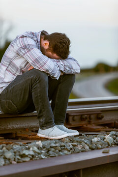 A young man sits on railroad tracks putting his head down in distress; Alberta, Canada