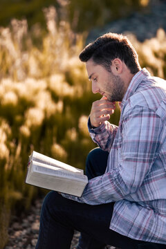 A young man reads from his Bible as he sits in the countryside; Alberta, Canada