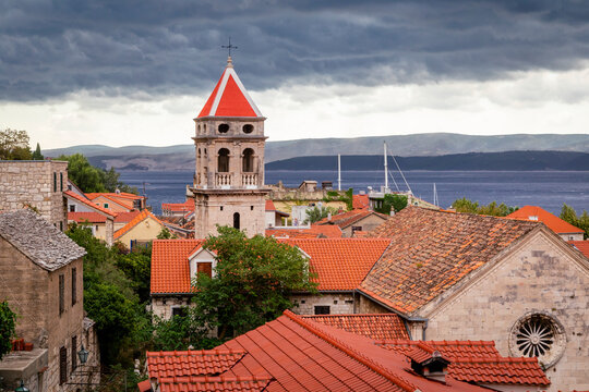 The bell tower of the Church of St Michael with the rooftops of the Old Town of Omis and grey clouds shadowing the Adriatic Sea; Omis, Dalmatia, Croatia