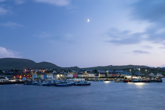 The small town of Portmagee and harbor at dusk with the quarter moon in the sky; Portmagee, County Kerry, Ireland