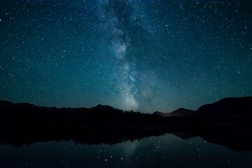 Milky Way and starry night sky over silhouetted mountains reflected in water, Waterton Lakes National Park; Alberta, Canada