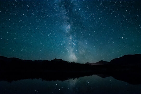Milky Way and starry night sky over silhouetted mountains reflected in water, Waterton Lakes National Park; Alberta, Canada