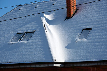 Closeup of house roof top with attic windows covered with snow in cold winter. Tiled covering of...