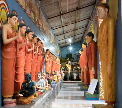 Hallway lined with statues of Standing Buddhas and sculptures of holy men sitting in front of them in the Buddhist Monastery of Galagoda Shailatharama Viharaya; Balapitiya, Galle District, Sri Lanka
