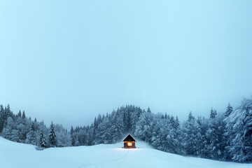 Fantastic winter landscape with glowing wooden cabin in snowy forest. Cozy house in Carpathian mountains. Christmas holiday concept