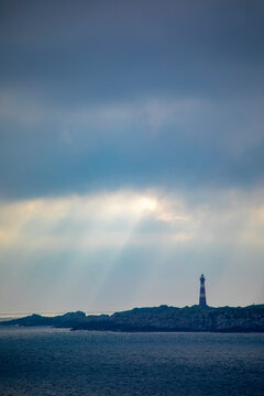 Hellisoy Lighthouse, a remote lighthouse on an island in the Western Fjords of Norway with sun rays reflecting through a stormy sky; Hordaland, Norway