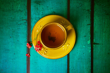 Yellow cup with black aromatic tea inside, red spindle shrub flower on saucer view from above. Mug...