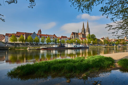 Outlook over the Danube River with the Gothic St Peter's Cathedral from the Marc​-Aurel-shore in the Old Town of Regensburg with a blue sky at sunset; Regensburg, Bavaria, Germany