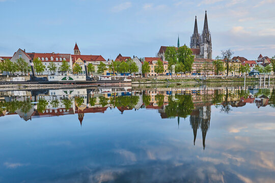 Outlook over the Danube River with the old, Gothic St Peter's Cathedral from the Marc​-Aurel-shore in the Old Town of Regensburg with a blue sky at sunset; Regensburg, Bavaria, Germany