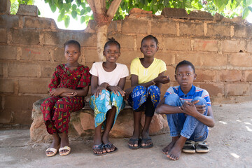 Group of clean and well-dressed children sitting neatly together in front of their parents' house...