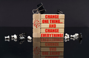 On a black reflective surface lie wooden blocks with the inscription - Change One Thing... and...
