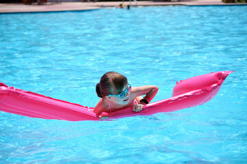 Young child girl falling in water from inflatable air mattress in swimming pool while swinnimg...