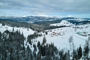 Winter landscape with small rural houses in remote settlement between snow covered forest in cold mountains