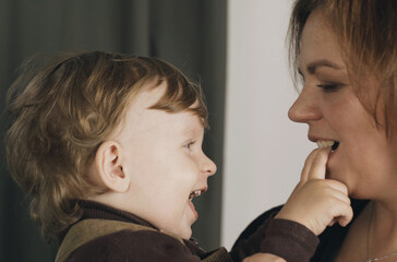 A little boy sits in his mother's arms, touches her face, smiles.
