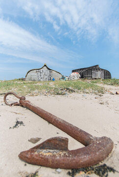 An anchor rests in the sand in front of upturned herring boats now used as fishing sheds on the Holy island of Lindisfarne, England.