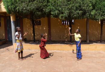 Three young African girls having fun with a makeshift ball on the street in front of their home;...
