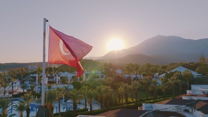 Fototapeta na wymiar Turkish flag at sunset against the backdrop of the hotel. Swimming pool and palm trees. Mountain