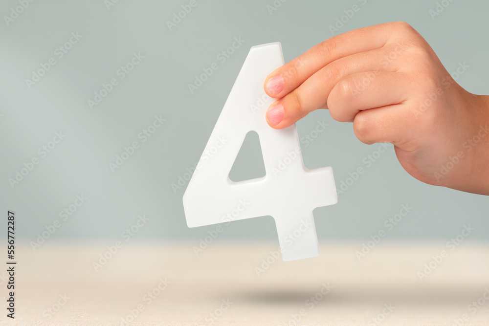 Aufkleber number four in hand. hand holding white number 4 on blurred background with copy space. concept with