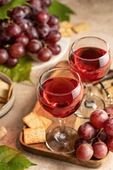 Two glasses of red wine, a bunch of red grapes, crackers and corkscrew on a wooden tray on beige textured background. Celebration party for two concept