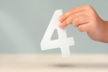 number four in hand. Hand holding white number 4 on blurred background with copy space. Concept with number four. Birthday 4 years, fourth grade, four day work week - obrazy, fototapety, plakaty
